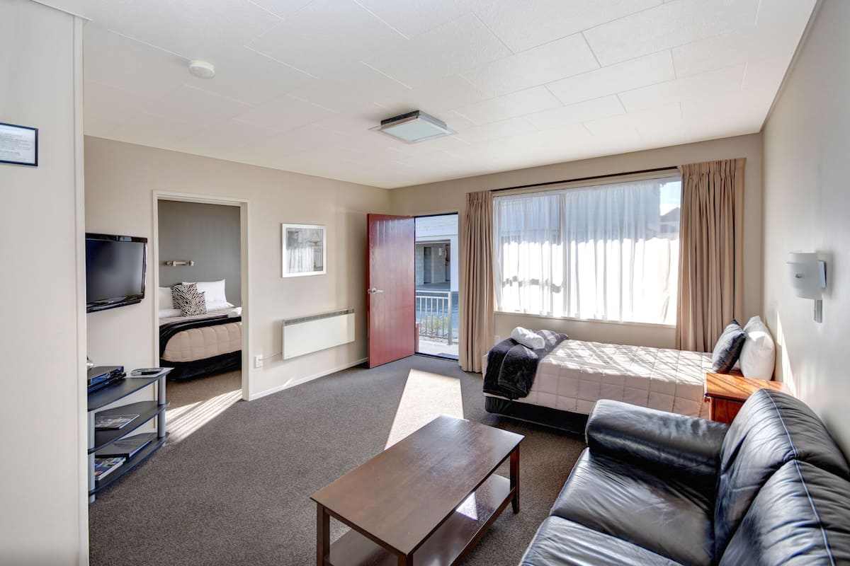 A hotel room with a bed, a sofa, a TV, a small table, and a window with curtains.