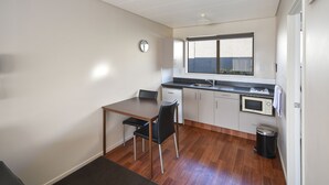 A compact kitchen with a dining area, a microwave, a sink, and a trash bin. - ASURE Adrian Motel (Dunedin)
