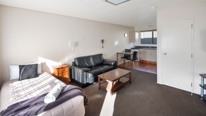 A modern hotel room with a bed, a sofa, a coffee table, a desk, and a kitchenette. - ASURE Adrian Motel (Dunedin)
