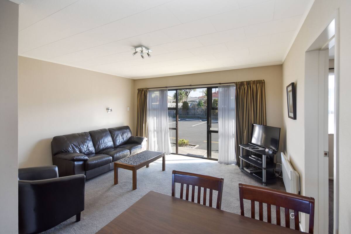 A living room with a sofa, coffee table, TV, and a dining table.