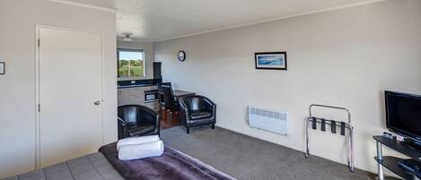 A room with a bed, a desk, a chair, a TV, and a window with a view of a green landscape.