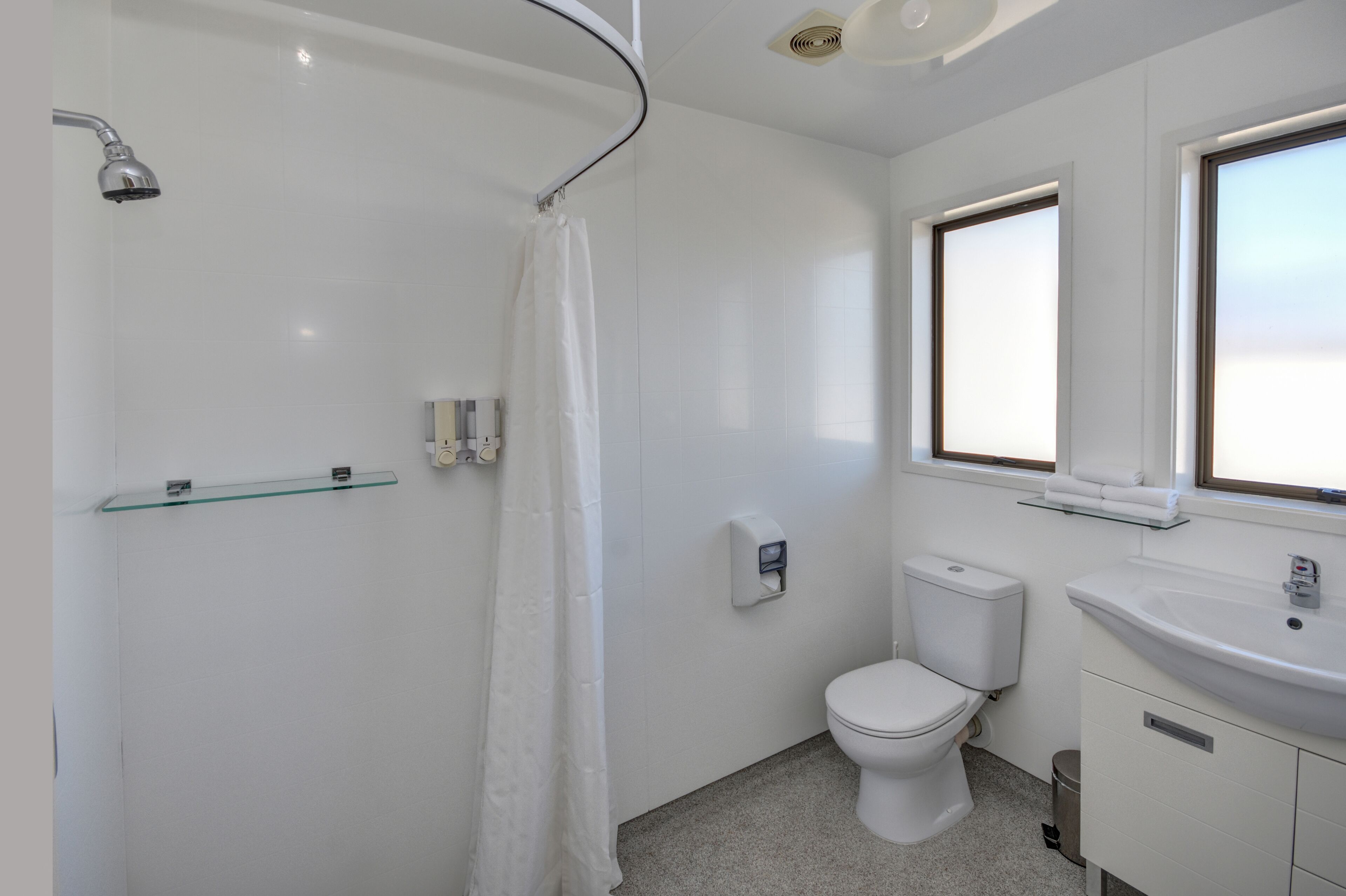 Een moderne badkamer met een douchecabine van glas, toilet, wastafel en een raam voor natuurlijk licht.
