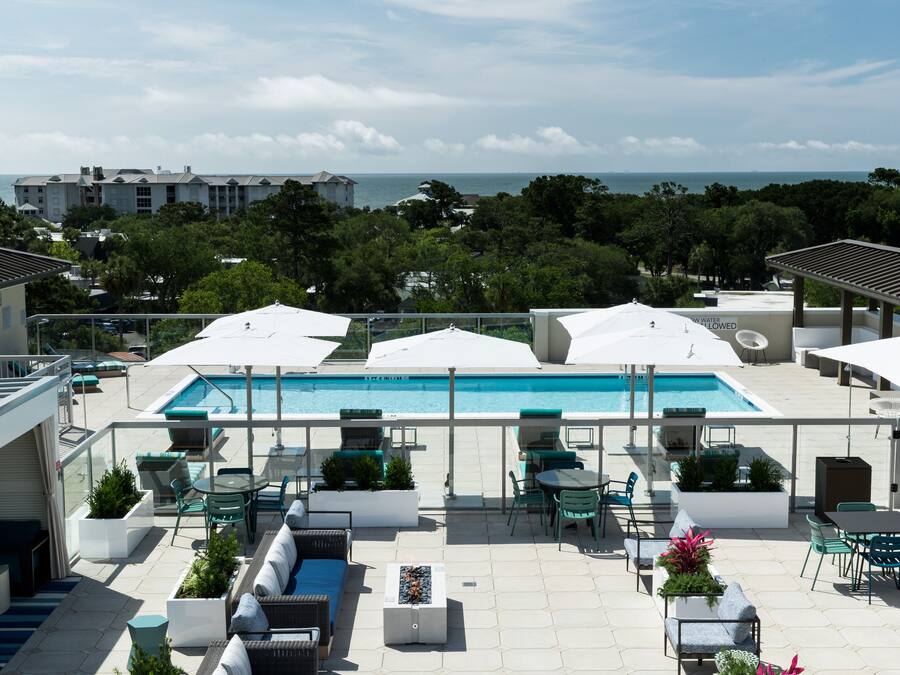 A rooftop pool area with outdoor seating and a view of the ocean.