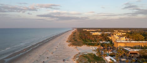 A beach with a long stretch of sand, a few buildings, and a clear sky.