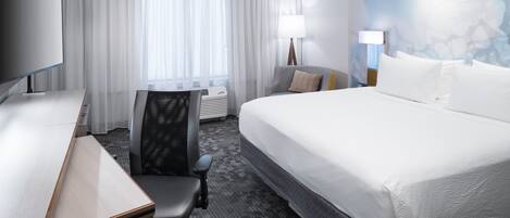 A hotel room with a large bed, a desk with a chair, a flat-screen TV, and a large window with curtains.