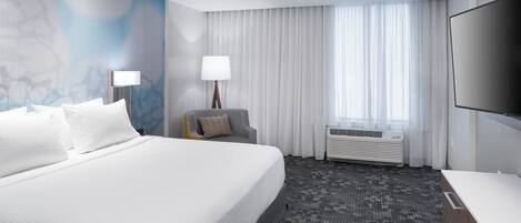 Hotelkamer met een groot bed, een bureau, een stoel, een televisie, een lamp en een raam met gordijnen.