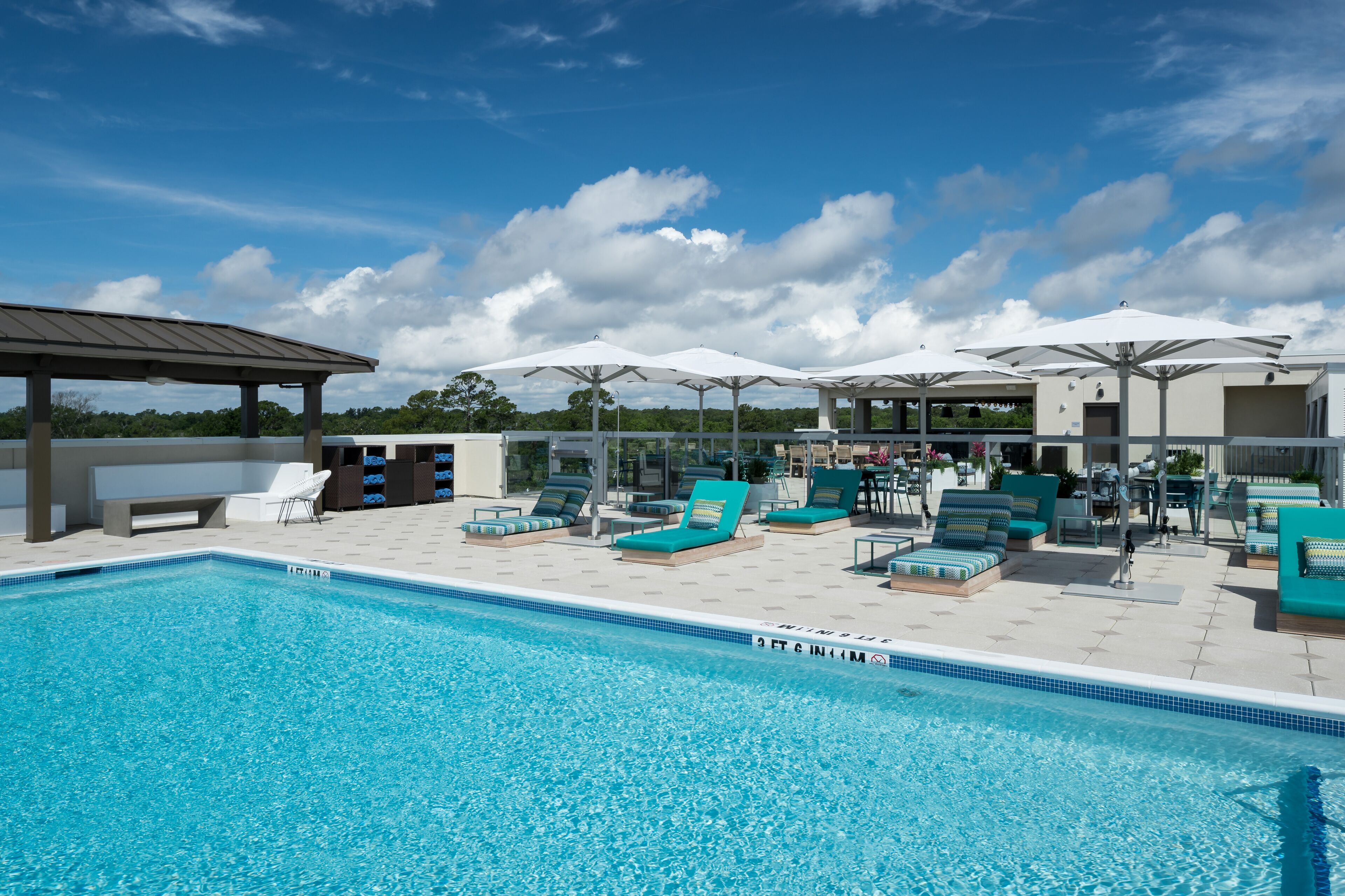 Uma piscina com espreguiçadeiras e guarda-sóis, rodeada por um espaço coberto com assentos.