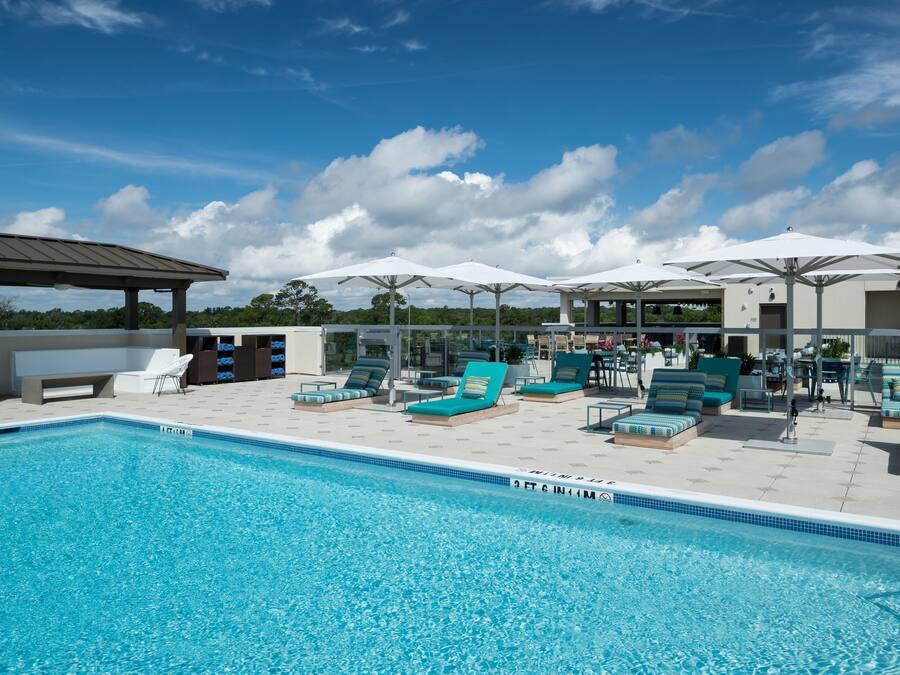 A swimming pool with lounge chairs and umbrellas, surrounded by a covered seating area.