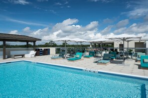 Une piscine entourée de chaises longues et de parasols, elle-même bordée d’un espace de repos couvert.