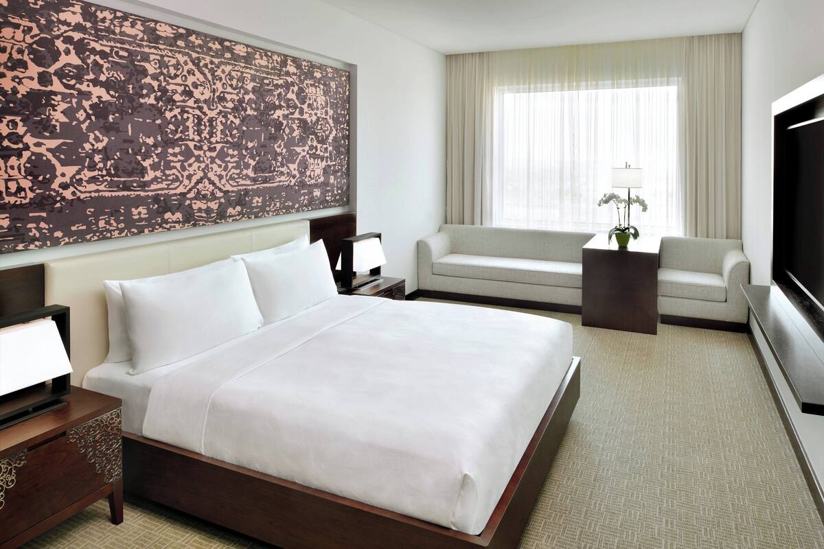 Una habitación de hotel con una cama grande, un sofá, un televisor y un adorno en la pared.