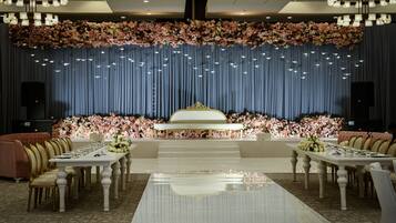 Een stijlvolle eetzaal met een lange tafel, stoelen en een podium met bloemversiering.