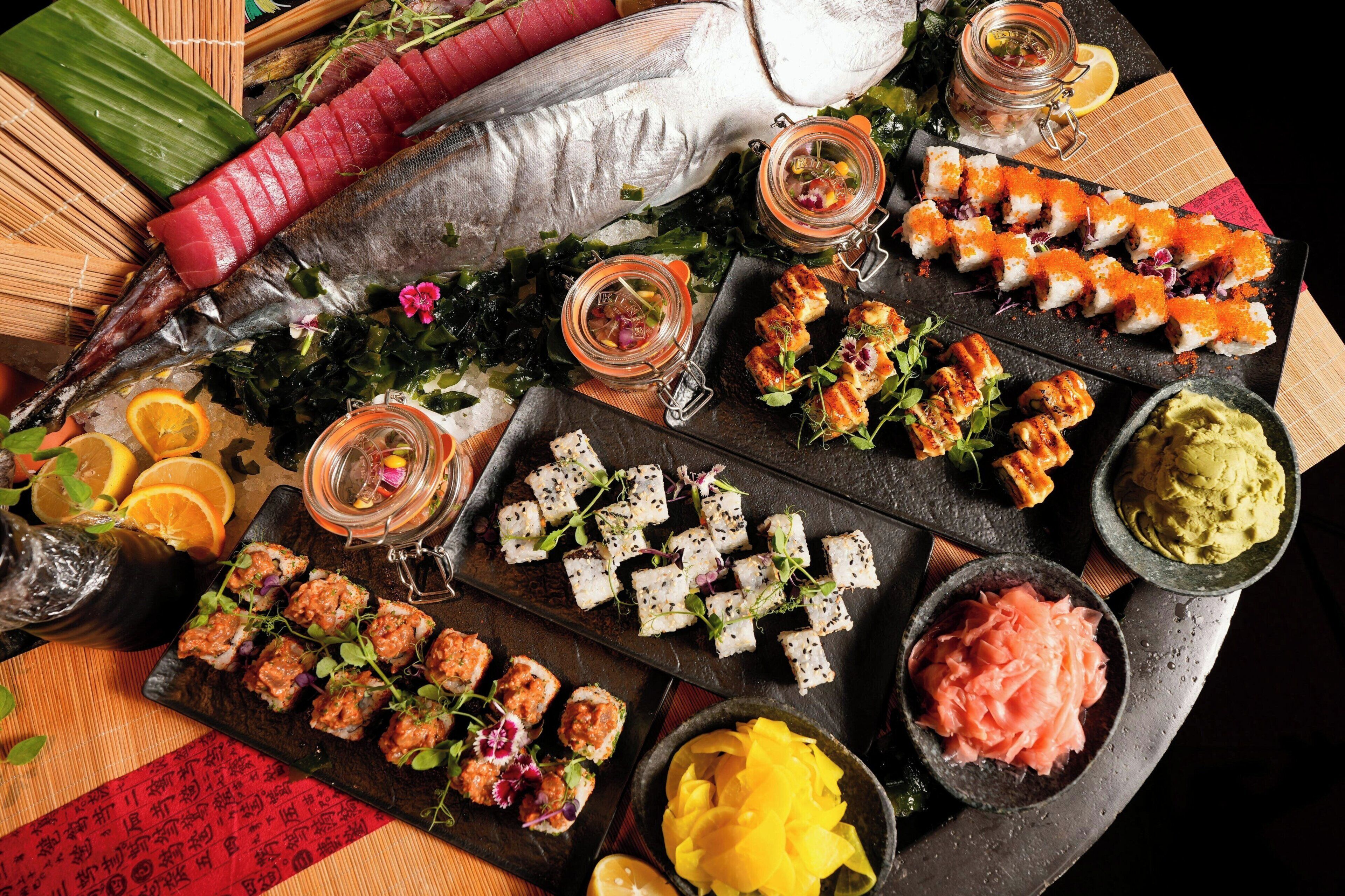 A variety of sushi and sashimi dishes on a black slate tray.