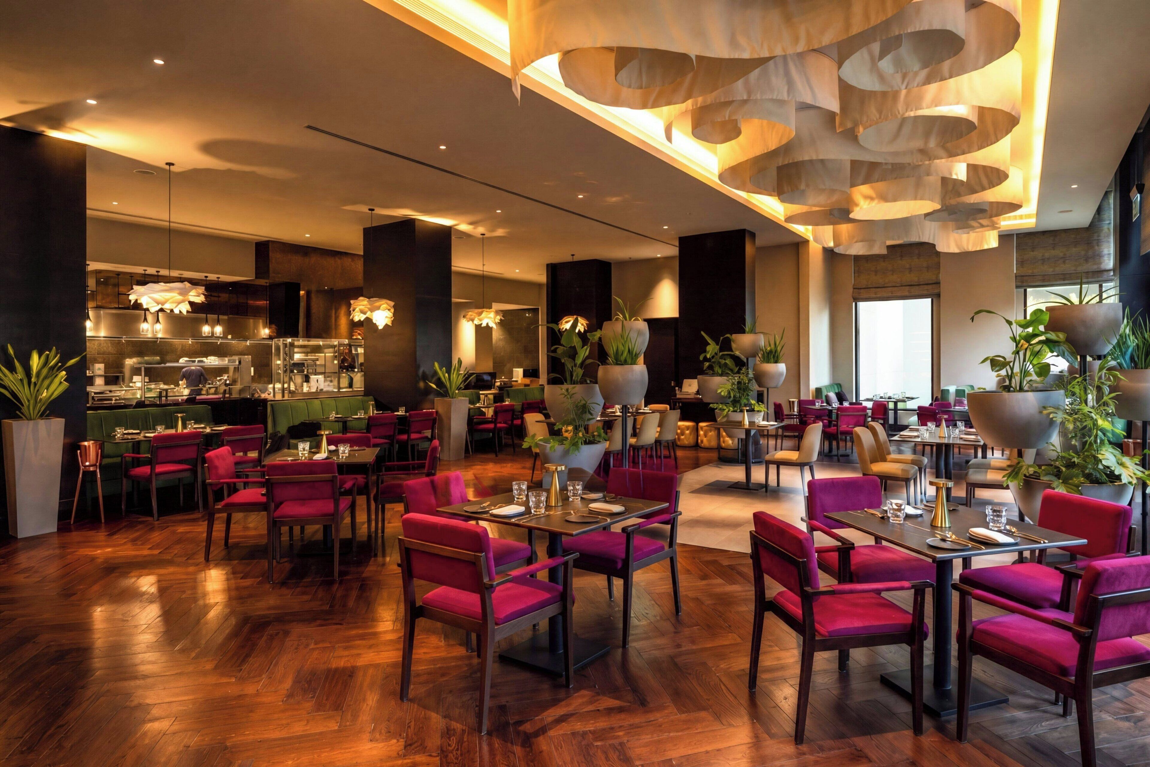 A spacious restaurant with wooden flooring, red upholstered chairs, and a modern ceiling design.