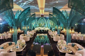 A spacious, elegantly decorated hotel lobby with a central reflective pool, seating areas, and distinctive green structural elements.