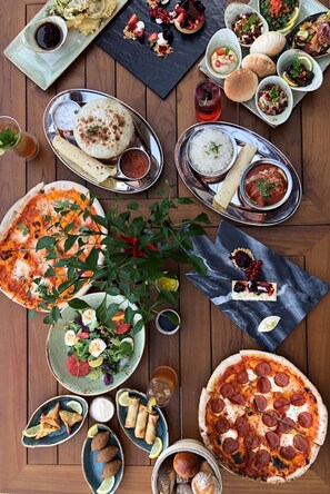 A variety of dishes including pizzas, salads, and bread, arranged on a wooden table.