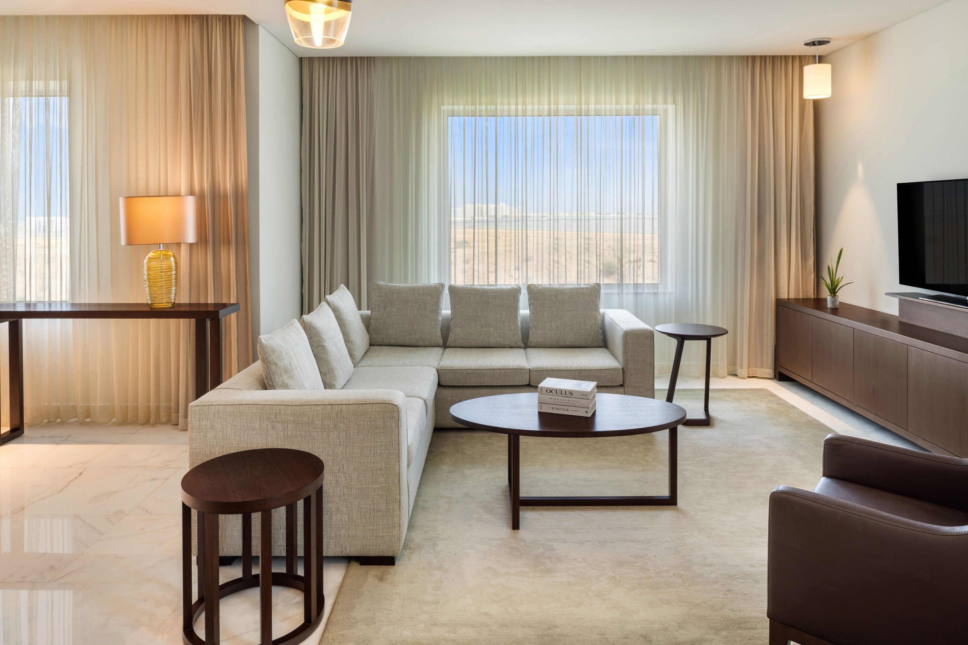 A modern hotel room with a sectional sofa, a small coffee table, a TV, and a view of the desert.