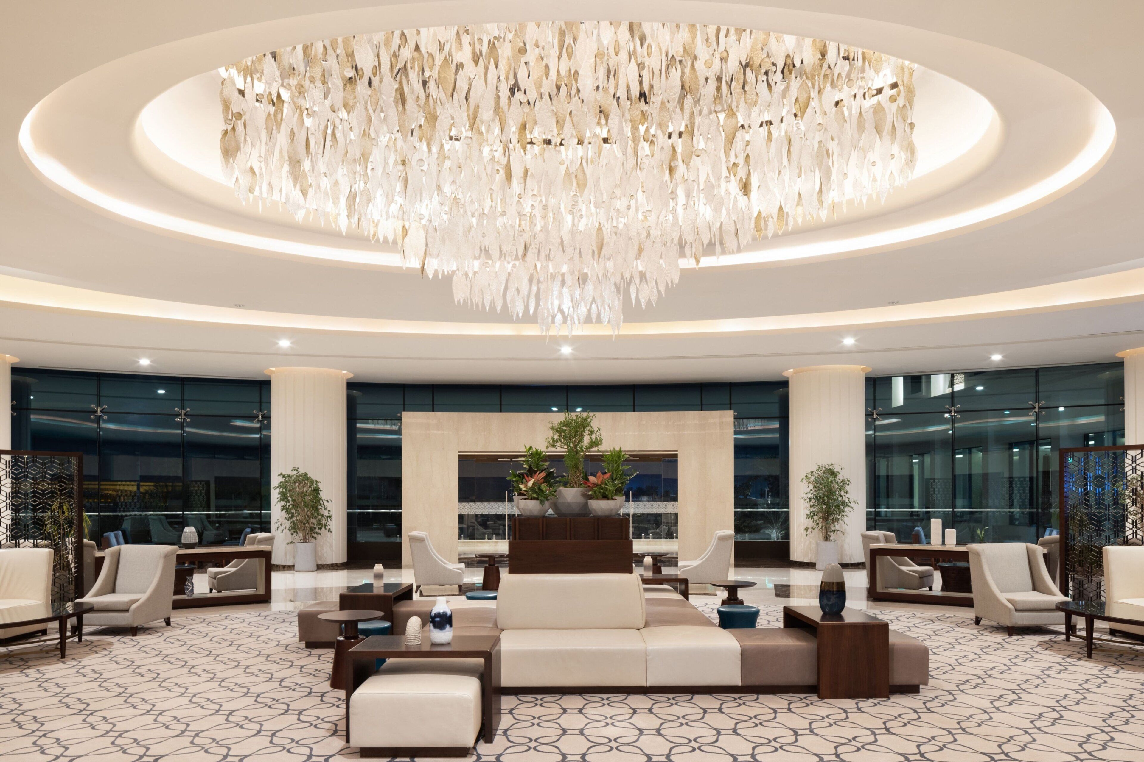 A spacious lobby with a modern chandelier, comfortable seating, and large windows.