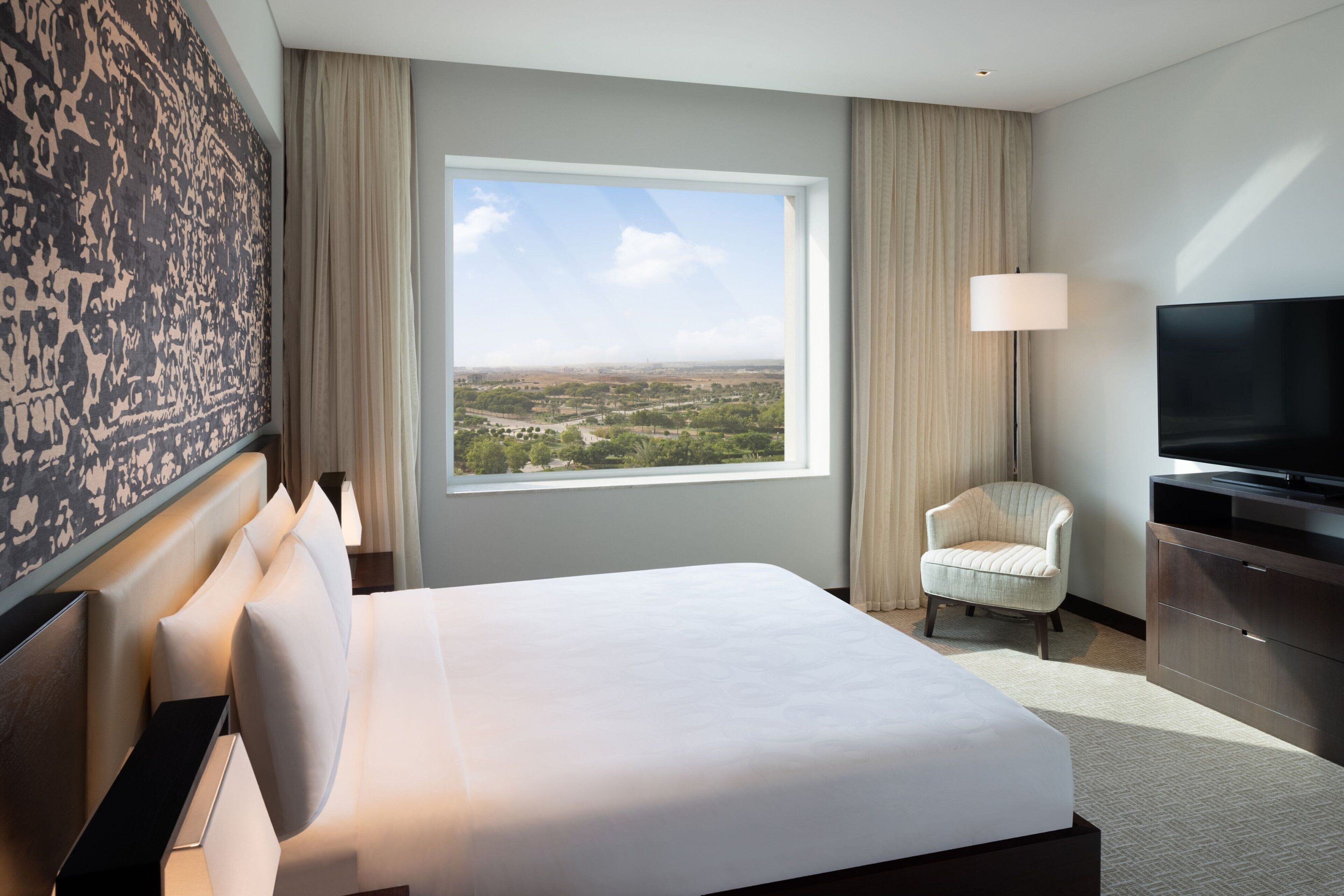 A hotel room with a large bed, a television, a chair, and a view of a landscape through a window.
