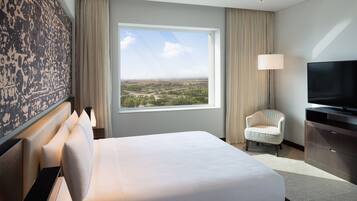A hotel room with a large bed, a television, a chair, and a view of a landscape through a window.