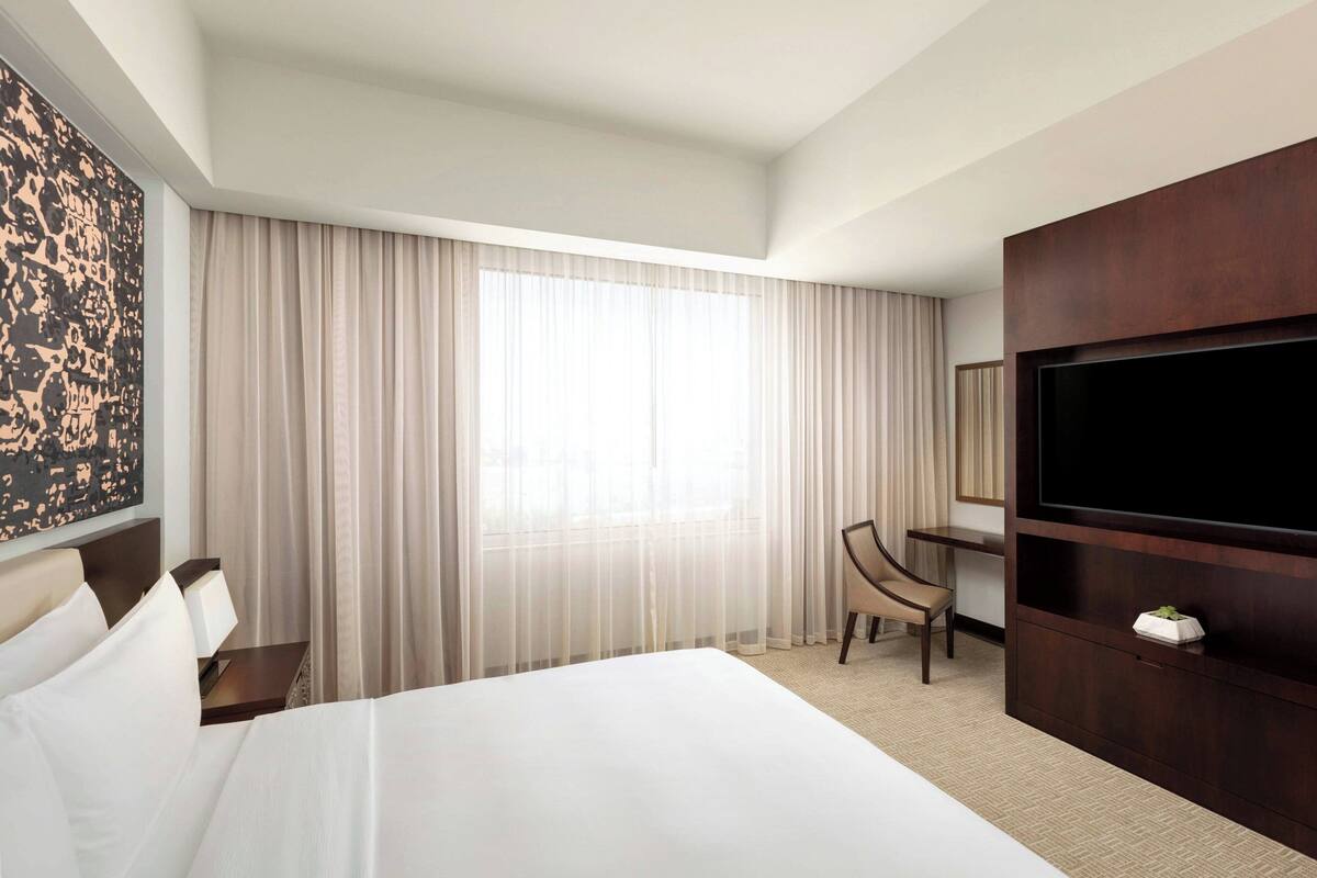 Habitación de hotel con una cama grande, un escritorio, una silla, un televisor y una ventana con cortinas.