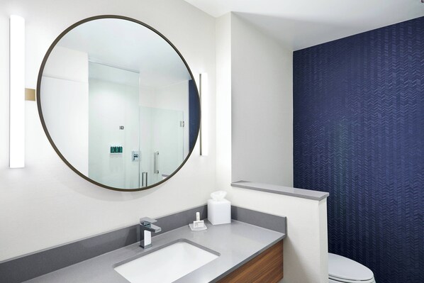 A modern bathroom with a large round mirror, a white sink, and a toilet. - Fairfield Inn & Suites by Marriott Sheboygan (Sheboygan)