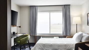 A hotel room with a bed, a desk, a chair, a TV, and a window with curtains.