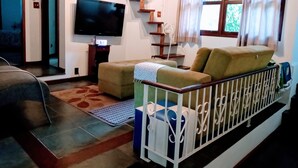 Una sala de estar con sofá, televisor, escalera y ventana con cortinas.
