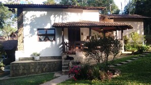 Un edificio blanco con techo de tejas, un porche y un pequeño jardín con flores y plantas.