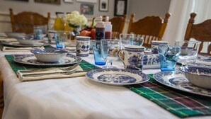 Taula de dinar preparada amb plats de motius blaus i blancs, vasos de vidre transparent i una placemat verda.