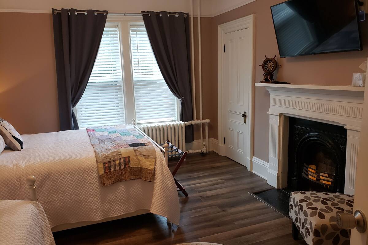 A bedroom with a bed, a fireplace, a television, and a window with curtains.