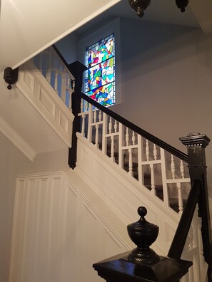 A staircase with white railings and a black balustrade, leading to a room with a stained glass window.
