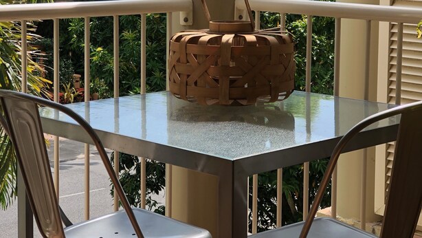 A balcony with a glass table and two chairs, overlooking a lush green landscape. - Port Douglas Apts on Macrossan Street (Port Douglas)