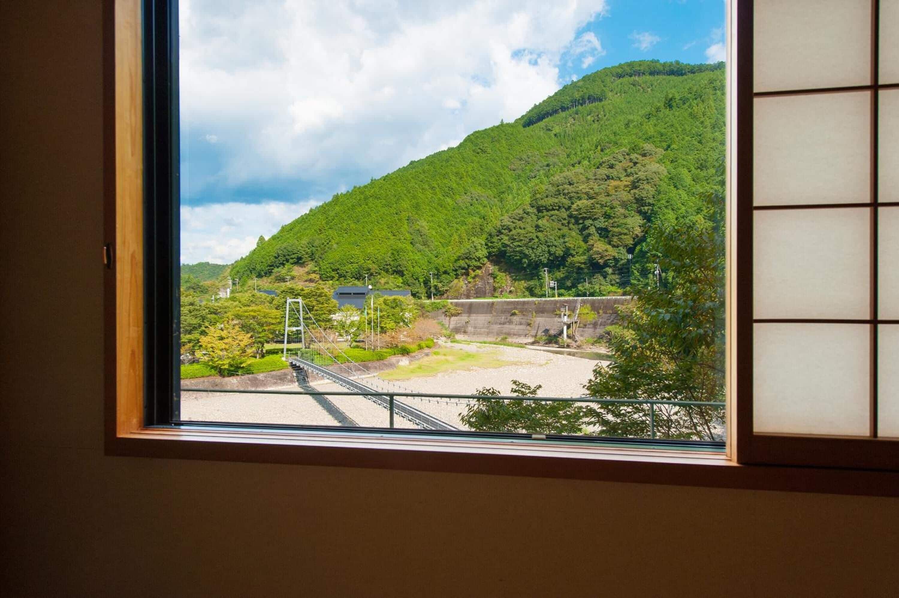 Blick durch ein Fenster auf eine gebirgige Landschaft mit einer Brücke und einem Gebäude.