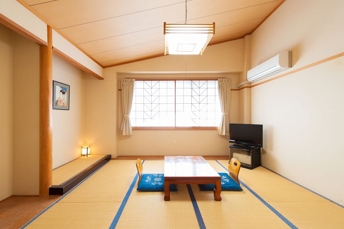 Una habitación japonesa tradicional con suelo de tatami, una mesa baja, un televisor y una puerta corredera.