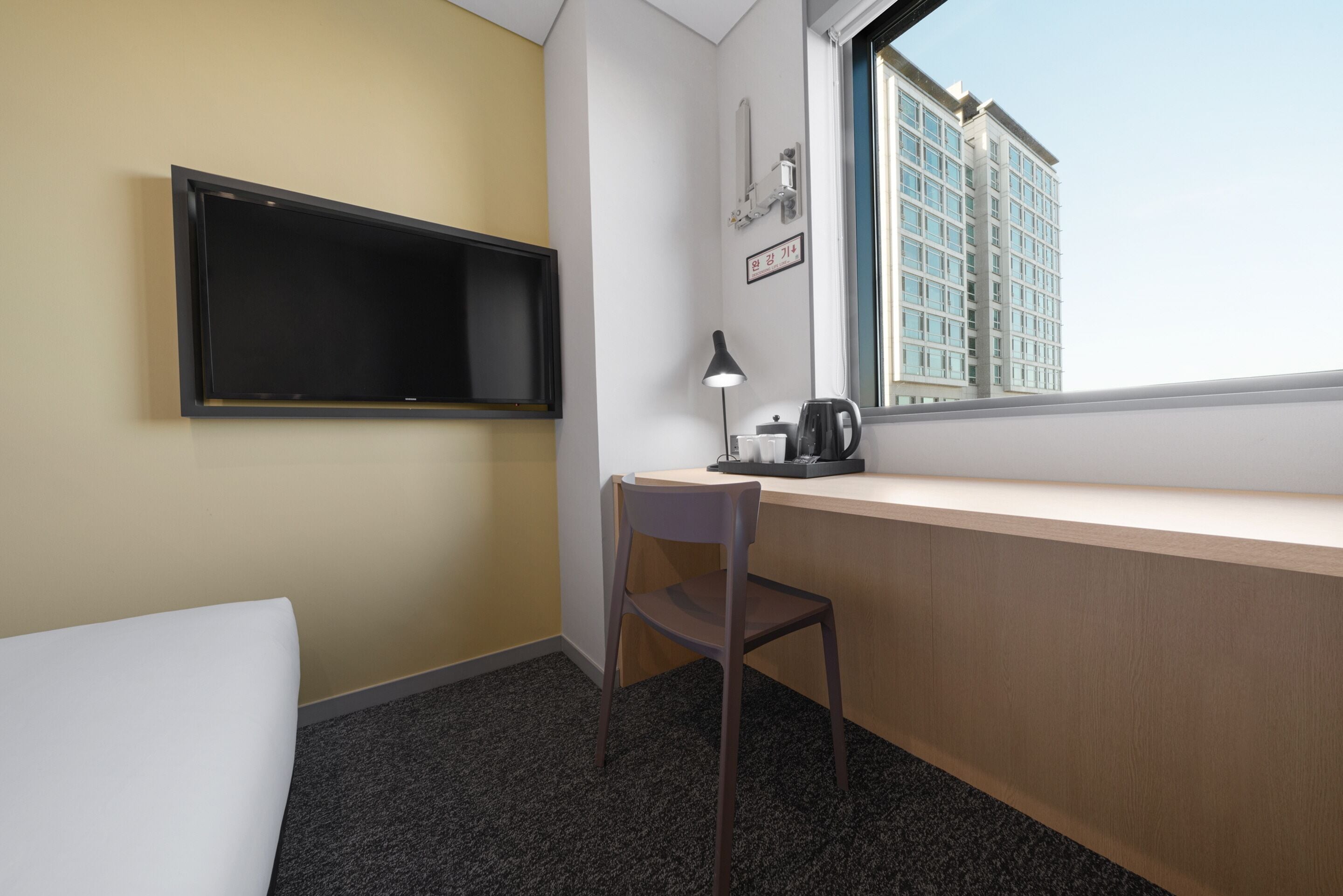 A hotel room with a desk, chair, and a window with a city view.