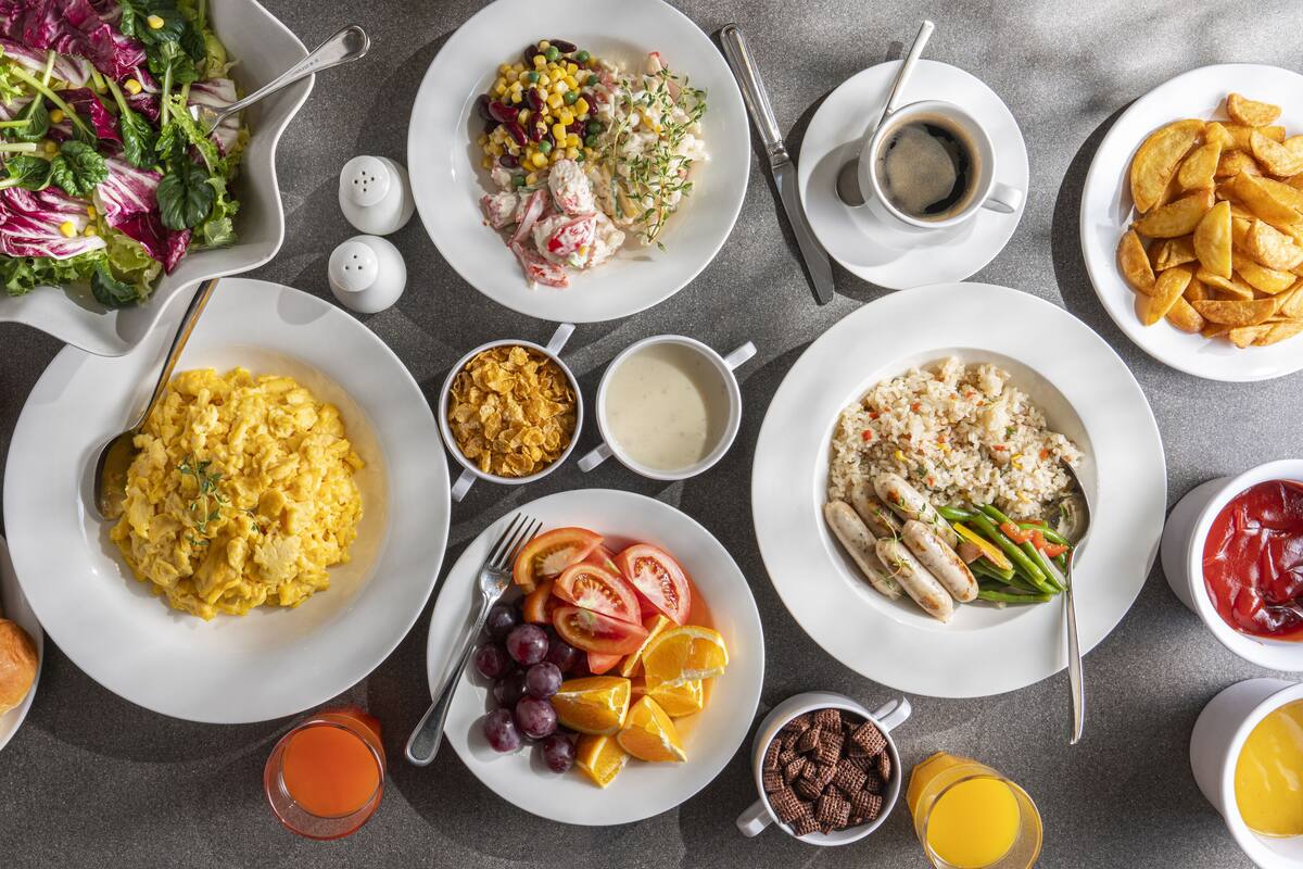 A table set with various breakfast items including scrambled eggs, toast, sausages, and a salad.