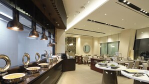 A modern hotel lobby with a buffet area, seating arrangements, and a large mirror.