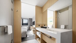 A modern hotel bathroom with a large mirror, a vanity with a sink, and a shower area.