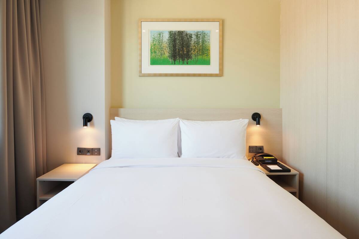 A neatly made bed with white linens, a framed artwork above it, and bedside lamps on either side.