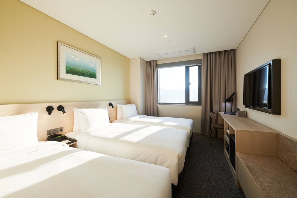 A hotel room with two beds, a TV, a desk, and a window with curtains.