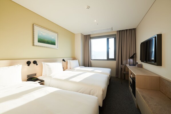 A hotel room with two beds, a TV, a desk, and a window with curtains.