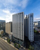 Un moderno edificio de hotel con un letrero destacado que dice "NINE TREE" y "BY PARNAS". Cuenta con una fachada de ventanas enrejada y una entrada central.
