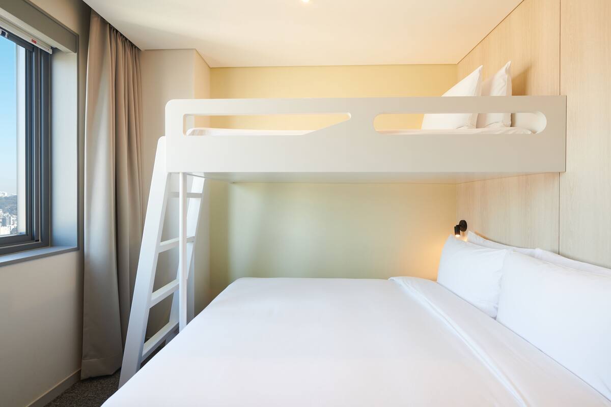 A bunk bed with a ladder, white bedding, and a headboard with a light fixture.