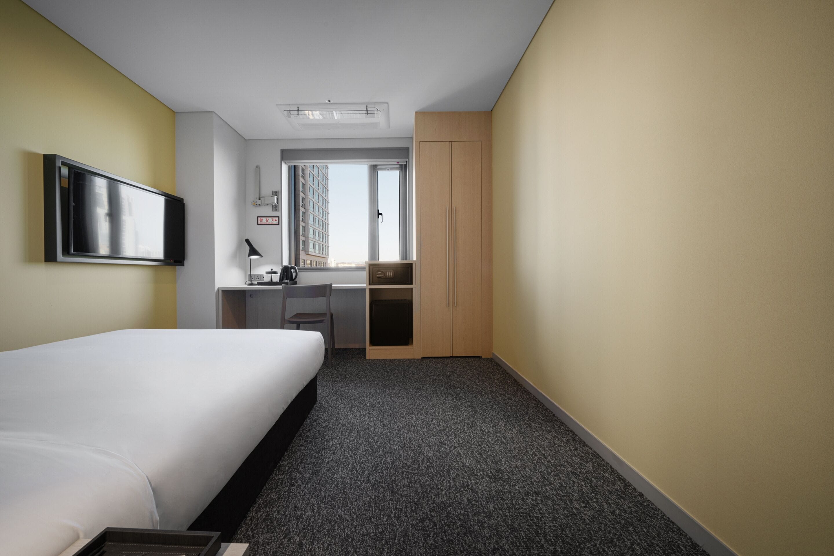 Ein Hotelzimmer mit Bett, Schreibtisch, Stuhl, Kleiderschrank und Fernseher an der Wand.
