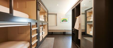 A modern hotel room with bunk beds, a bench, and a walk-in closet.