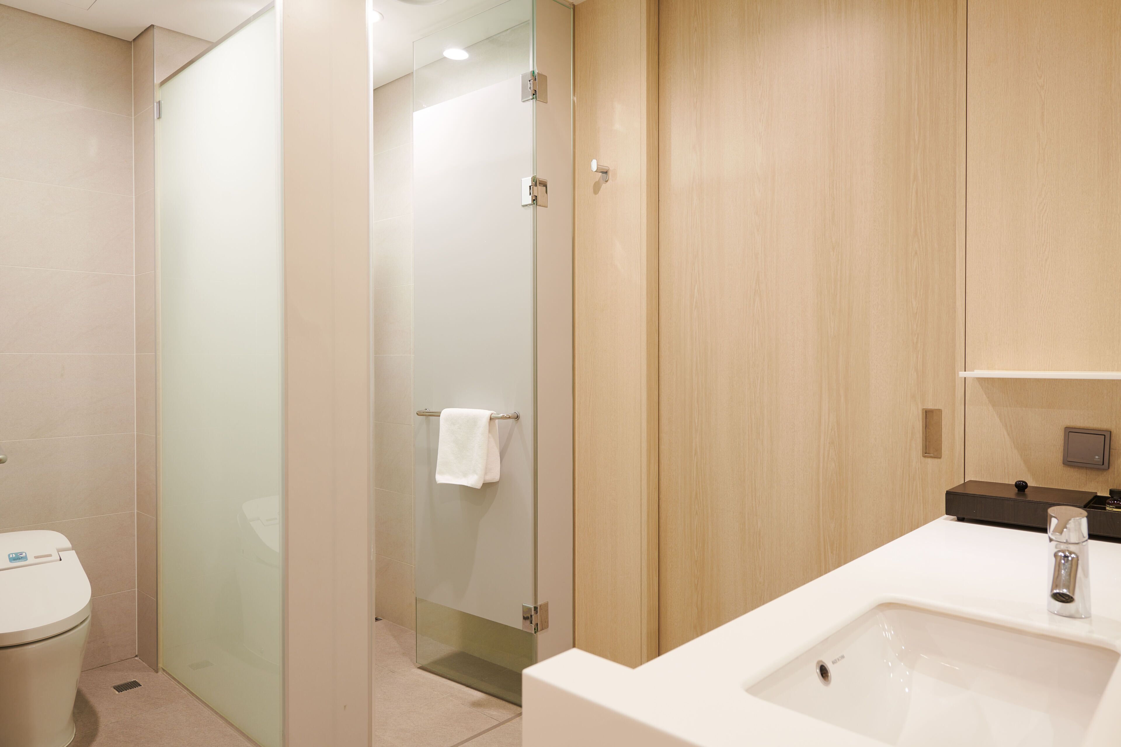 Een moderne badkamer met een douchecabine van glas, een wit wastafeltje en houten kastjes.