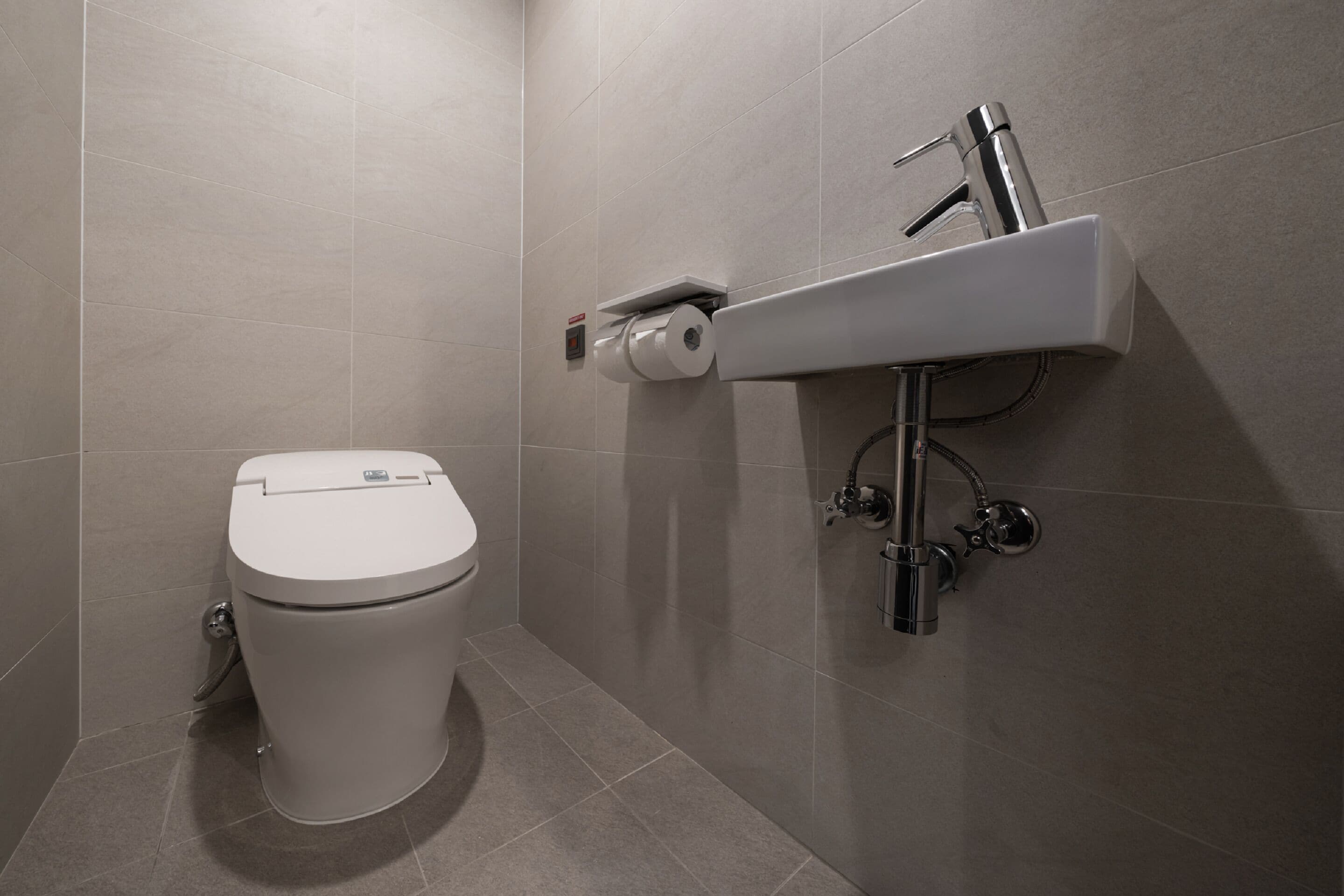 Un baño moderno con inodoro, lavamanos empotrado y dispensador de papel higiénico.