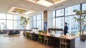 A modern office space with a long table, multiple chairs, and large windows offering a city view.
