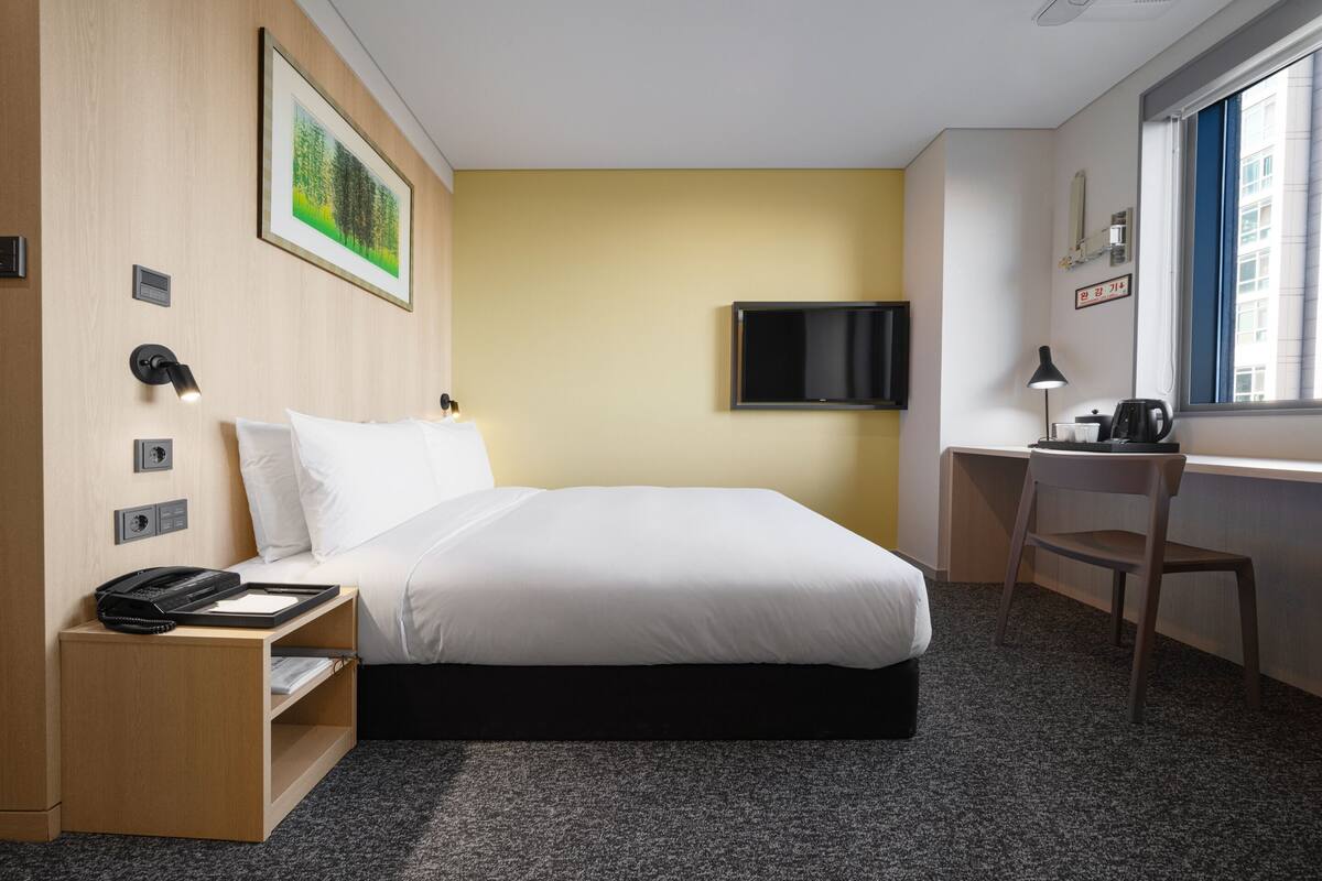 A hotel room with a bed, desk, chair, and a TV on the wall.