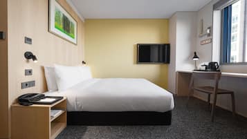 A hotel room with a bed, desk, chair, and a TV on the wall.